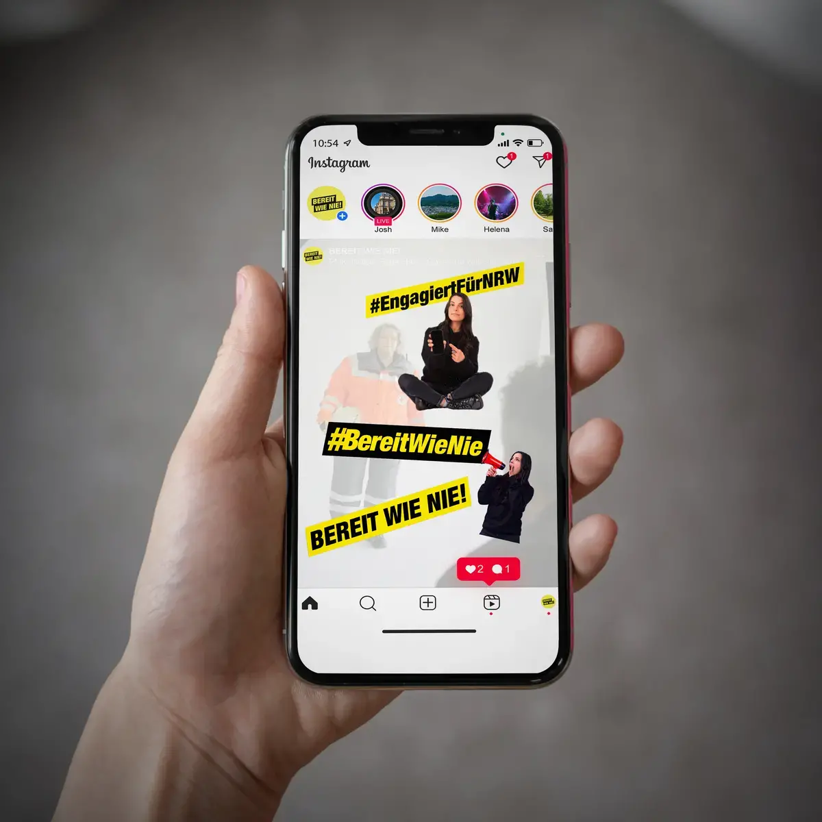 Das Bild zeigt eine Hand, die ein Smartphone hält. Auf dem Screen ist ein Social Media Posting, welches die Sticker benutzt.