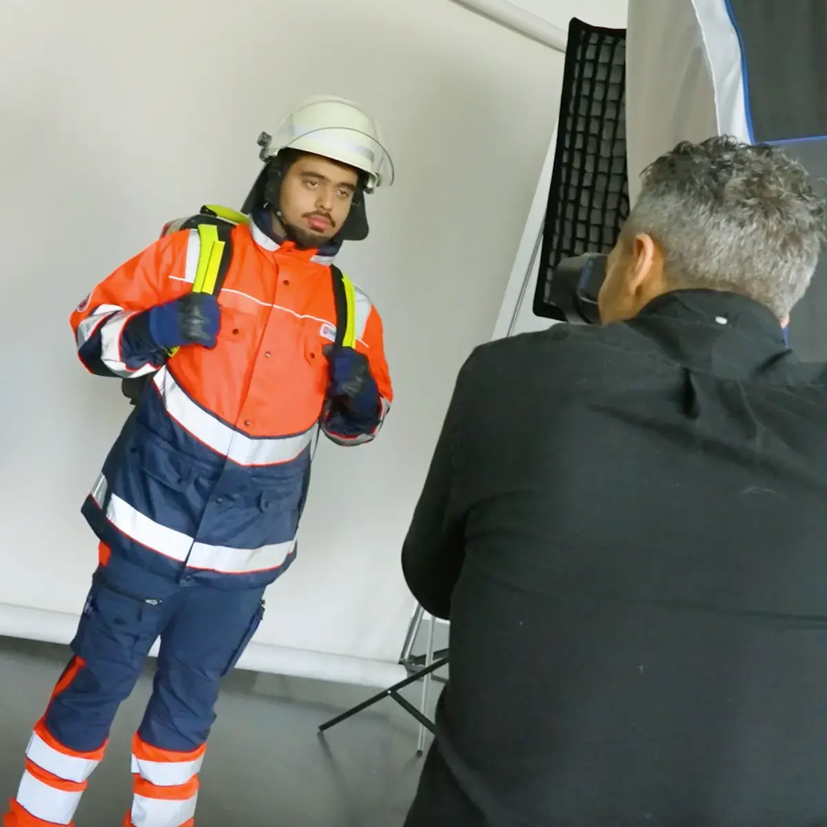 Das Bild zeigt einen jungen Mann, der von einem Fotografen fotografiert wird. Er trägt eine rote Malteser-Einsatzkleidung.