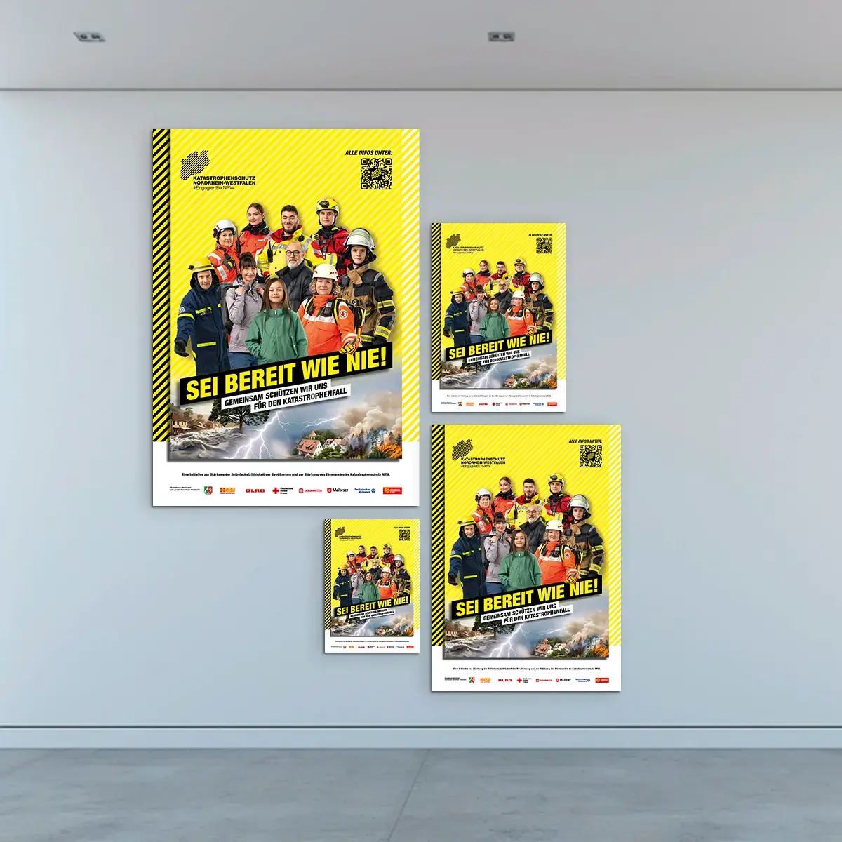 Das Bild zeigt eine Gruppenansicht des gleichen Posters. Auf dem Poster: Eine Gruppe aus Katastrophenschützerinnen und Zivillisten stehen vor einem gelben Hintergrund. Auf den Bildern steht der Slogan &quot;SEI BEREIT WIE NIE!&quot;